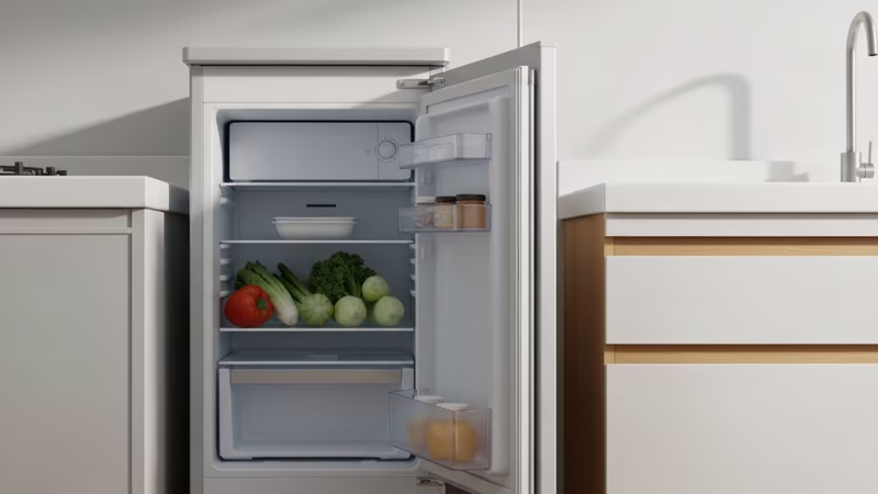 日本の賃貸アパートの明るいキッチンで、フレームを占める一人暮らし用冷蔵庫。開いたドアから整頓された野菜が覗く